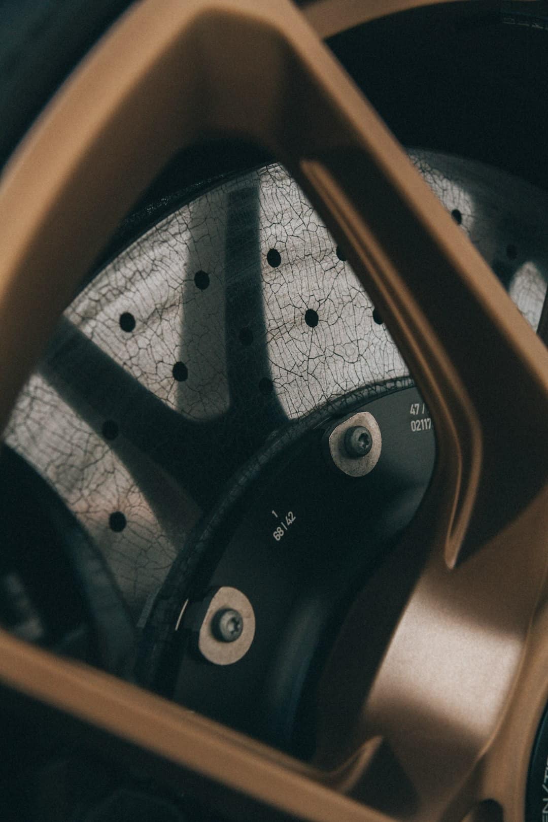 Worn car brake disc behind bronze wheel spokes.